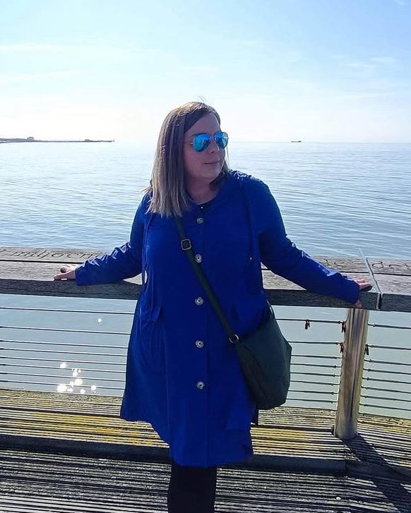 Woman in a blue coat standing on a wooden pier by the water
